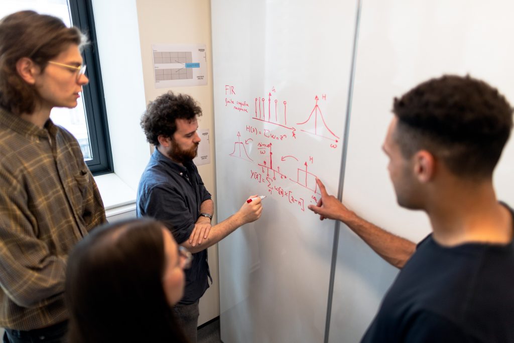 A group of scientists discuss equations at a whiteboard